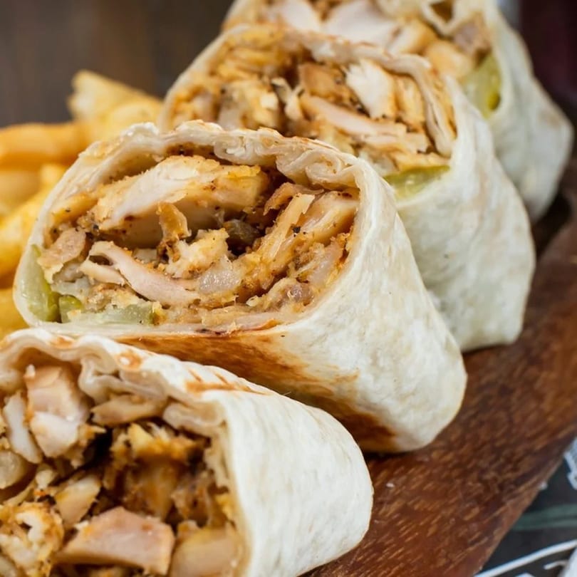 Four chicken shawarma wraps, cut in half, revealing seasoned chicken and pickles, served with fries.