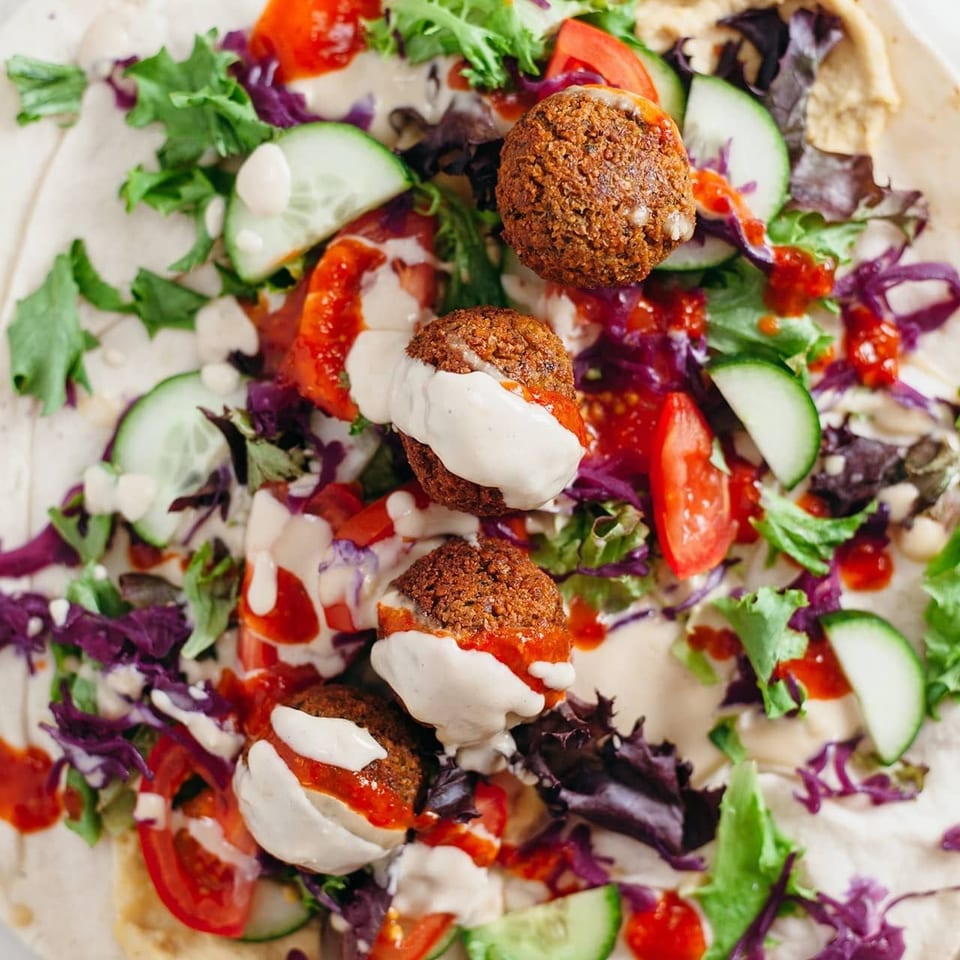 Overhead view of a falafel wrap with fresh vegetables, hummus, and sauces on a tortilla.